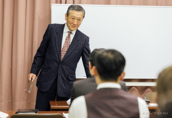 経営者向けの勉強会で、講師が参加者に語りかけながら、右手と左手の役割を例に経営の本質を伝えている講義風景。