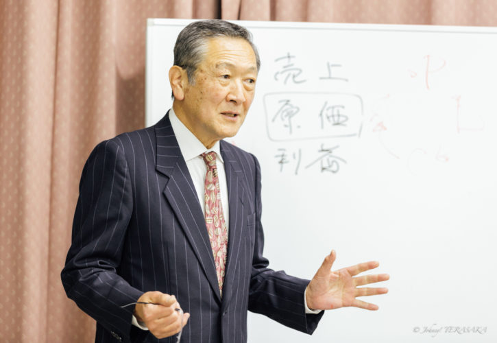 経営の真理について陰陽思想をもとに語る講師が、ホワイトボードの前で参加者に向けて講義を行っている様子