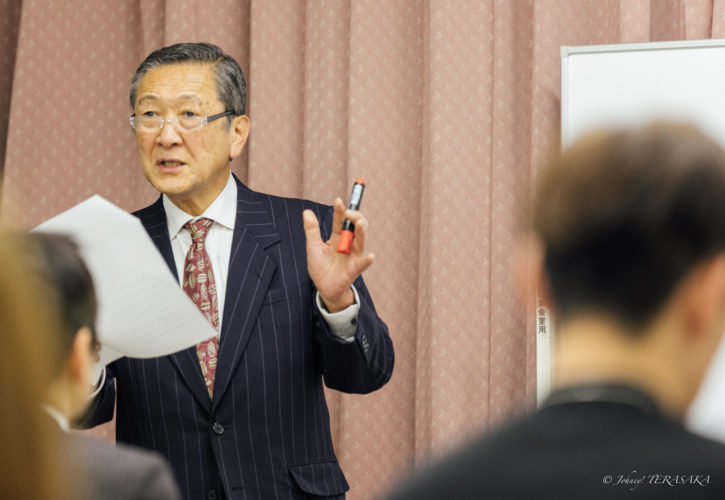 経営講座にて、規範と組織運営について説明する講師の姿。資料を手に、参加者に向けてPDSの考え方を語っている様子。