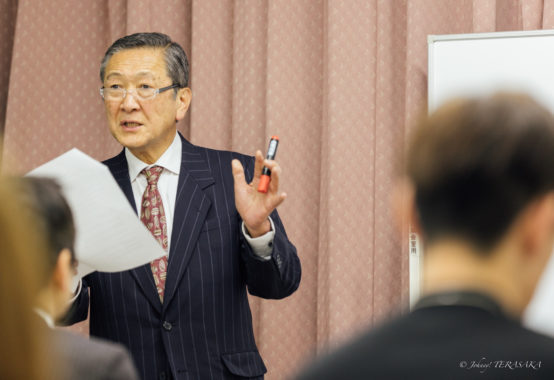 経営再建と善意の力について語る講師が、資料を手に参加者へ説明している様子