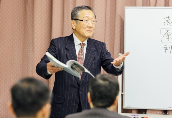 講師が資料を手に、受講者に向けて経営の真理について説明している講話の様子