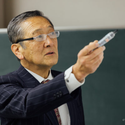 ホワイトボードに向かい、ペンを手に取りながら真剣な表情で要点を示す講義中の講師