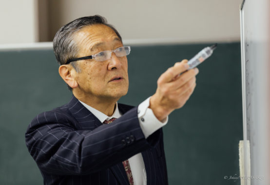 ホワイトボードに向かい、ペンを手に取りながら真剣な表情で要点を示す講義中の講師