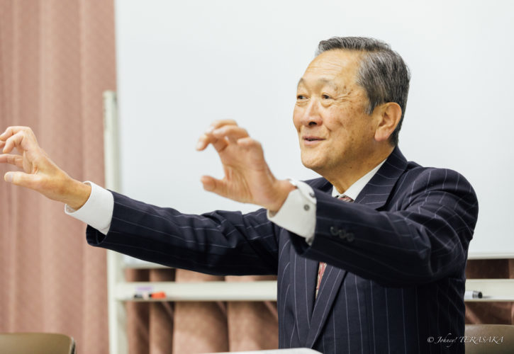 経営の本質について両手を広げながら語りかける講師の姿。参加者に向けて全体像と流れを伝えている講義風景。