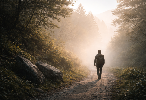 朝日の中で山道を静かに歩きながら荷を担ぐ人物の姿が、挑戦を続けることで荷が軽くなる心の真理を象徴している情景